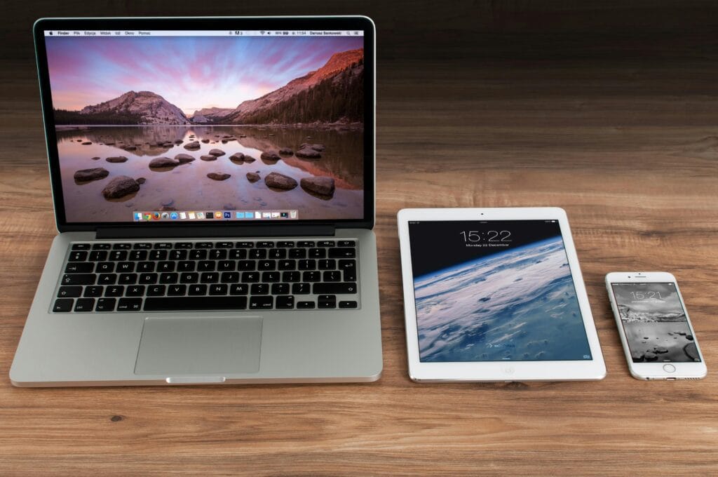 apple-iphone-smartphone-desk-4158 Modern workspace showcasing Apple laptop, tablet, and smartphone on a wooden desk.