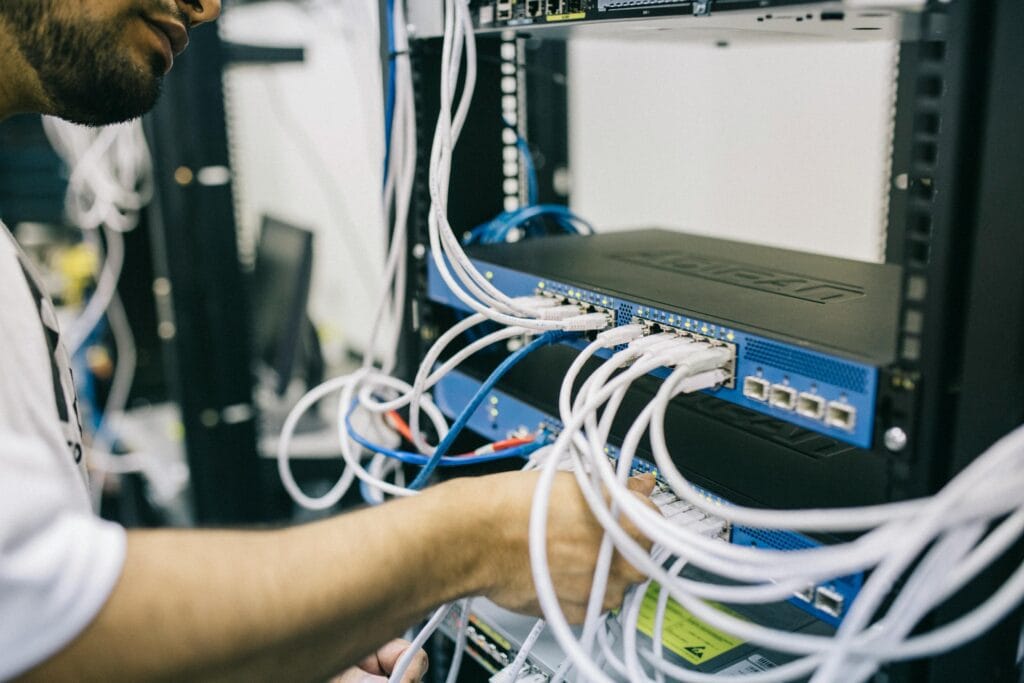 pexels-photo-442150-442150 An IT professional configuring network cables in a server rack, focusing on Ethernet connections.