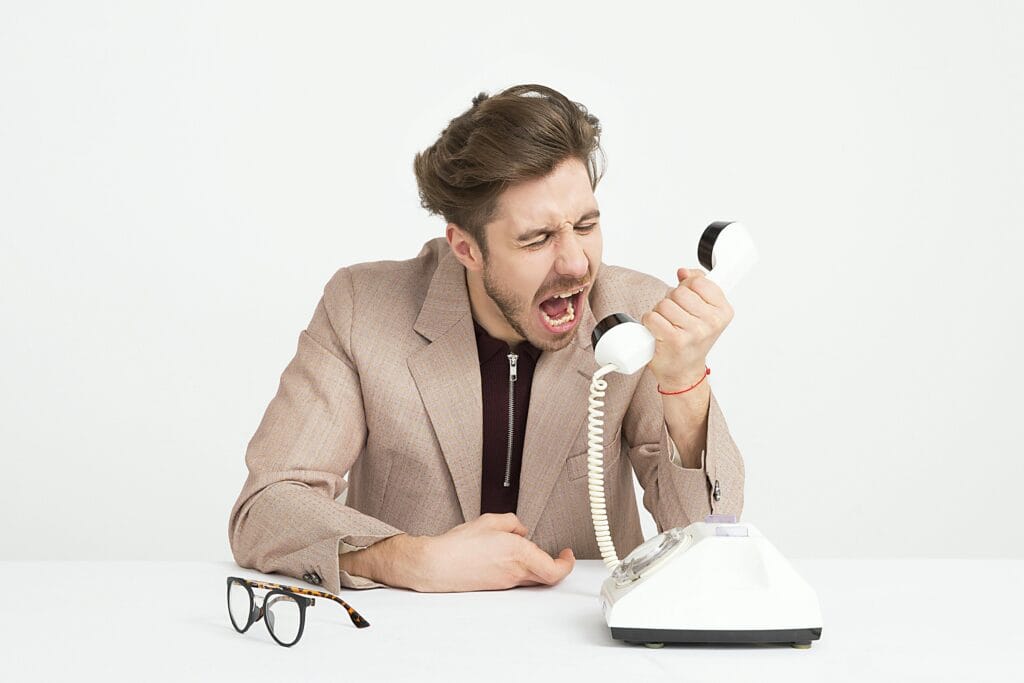 pexels-photo-1587014-1587014 Businessman in a beige suit shouting into a vintage telephone, expressing frustration at work.