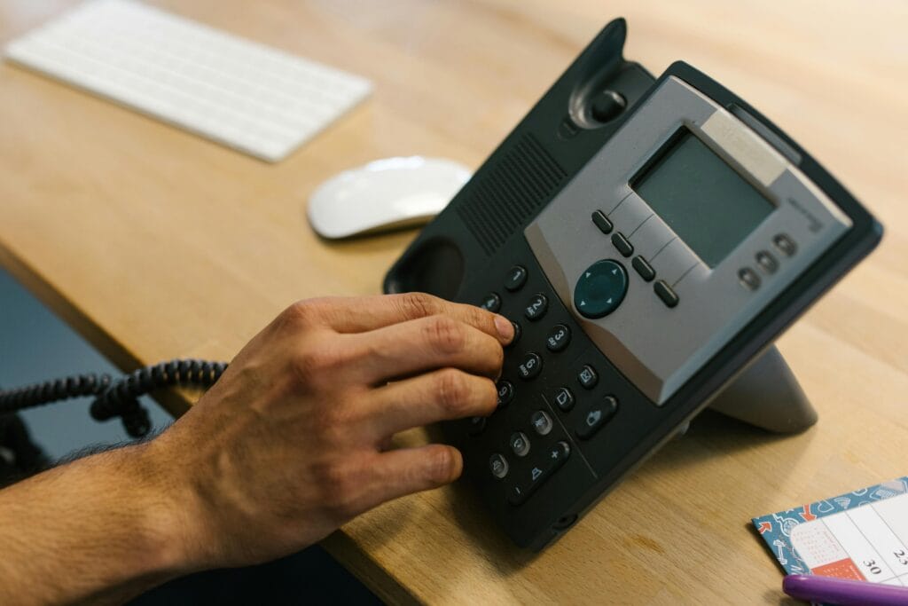 pexels-photo-7580908-7580908 A hand dialing a phone on a wooden desk. Office environment with keyboard and planner.